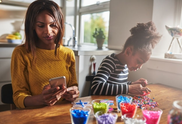 Mother sitting at table looking at phone next to a child