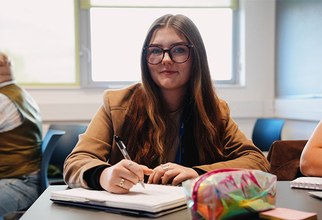 Staff member sat at table with notebook and pen