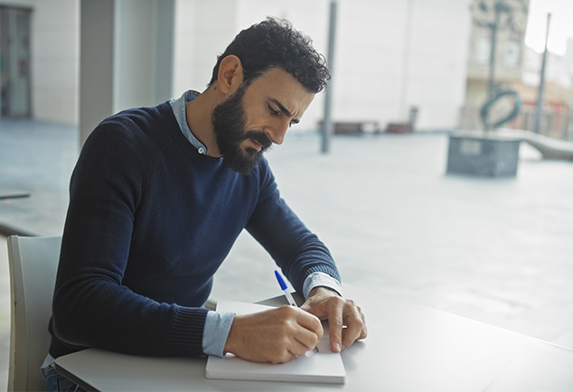 Man writing in notebook whilst sat at table