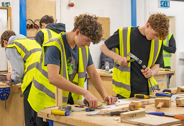 Carpentry students working in workshop using hammers and saws