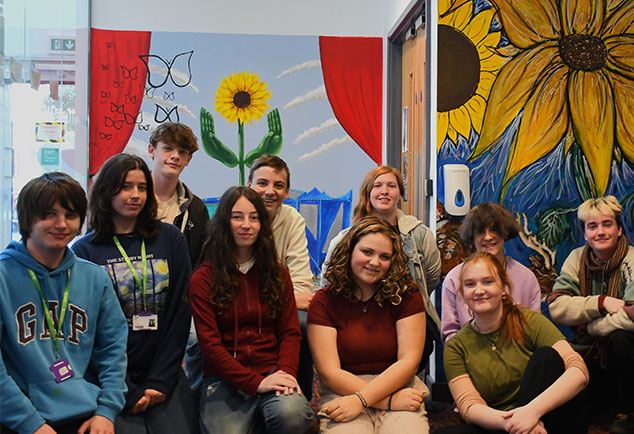 Group of students posing for photo in front of mural