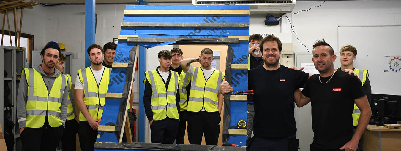 Group of students standing next to a roof frame inside a workshop